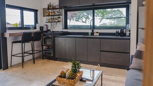 A modern kitchen with a large window, a built-in shelf with kitchen items, and a dining area with a table and chairs. - Ocean View Private Studio, Le Suite Santa Teresa (Provincia de Puntarenas)