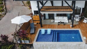 A rooftop pool area with a wooden deck, white outdoor furniture, and a large pool. - Ocean View Private Studio, Le Suite Santa Teresa (Provincia de Puntarenas)
