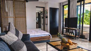 A modern bedroom with a large bed, a sofa, a television on a stand, and a fruit basket on a coffee table. - Ocean View Private Studio, Le Suite Santa Teresa (Provincia de Puntarenas)