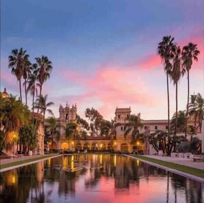 Un patio con un estanque reflectante, palmeras y un edificio de estilo arquitectónico tradicional.