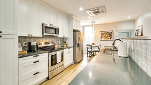 A modern kitchen with white cabinets, stainless steel appliances, and a marble countertop.