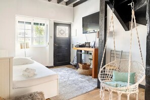 Relax in a serene bedroom with a neatly made bed, a hanging chair, and a desk with a flat-screen TV.