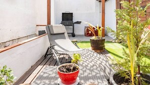 A patio with a lounge chair, a small table with a potted plant, and a grill area in the background. - BBQ, Easy Parking & near Tejo, Lisbon Garden Stays (Lisboa)