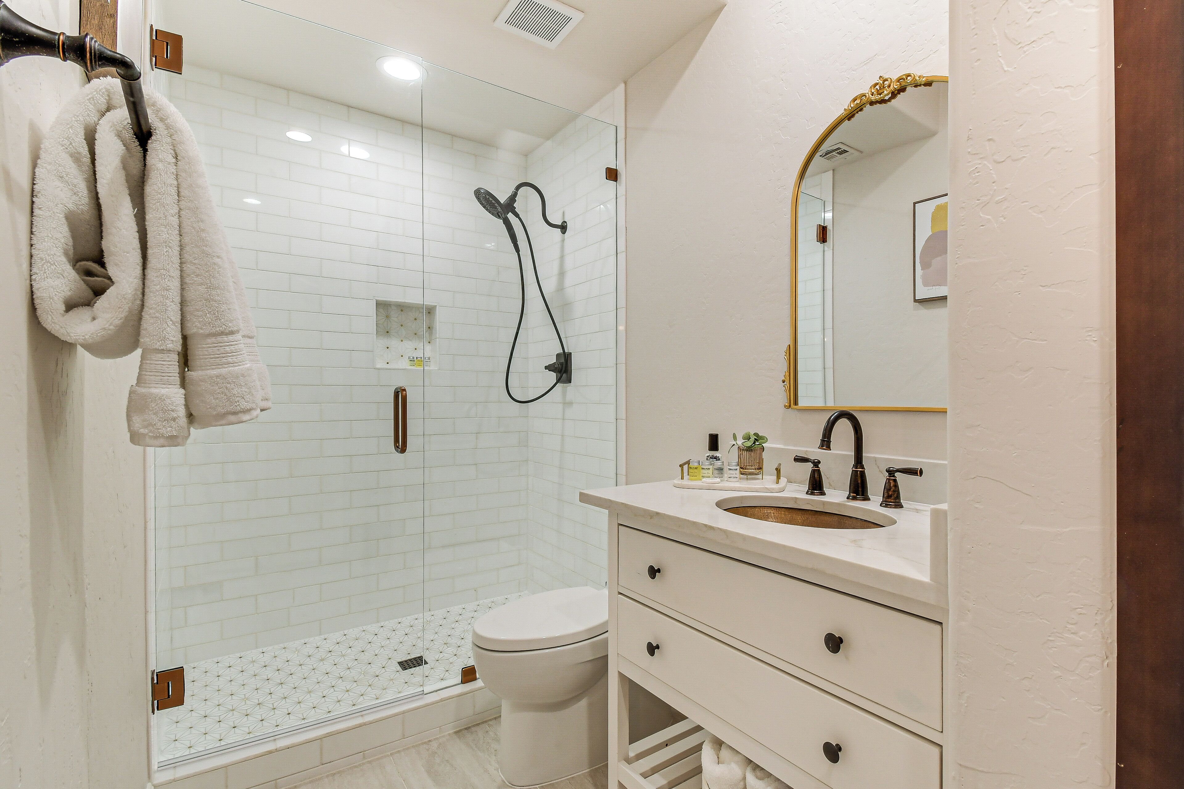Un bagno moderno con doccia vetrata, un water bianco, un lavabo con mobile e uno specchio con cornice decorata.