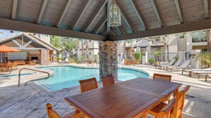 A pool area with a wooden table and chairs, a stone pillar, and lounge chairs. - Scottsdale Extended-Stay Condo w/ Pool Access (Scottsdale)