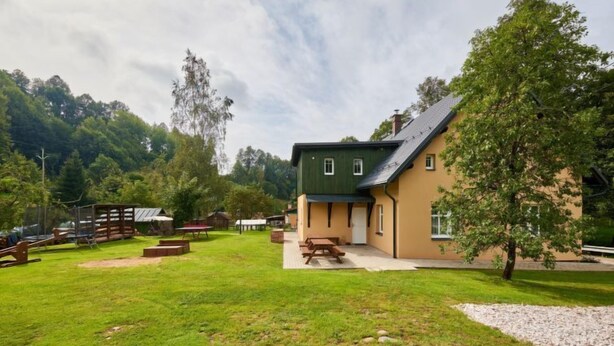 A building with a green roof and beige walls, surrounded by a grassy area with picnic tables and a wooden deck. - Apartment Meda by Interhome (Rudnik)