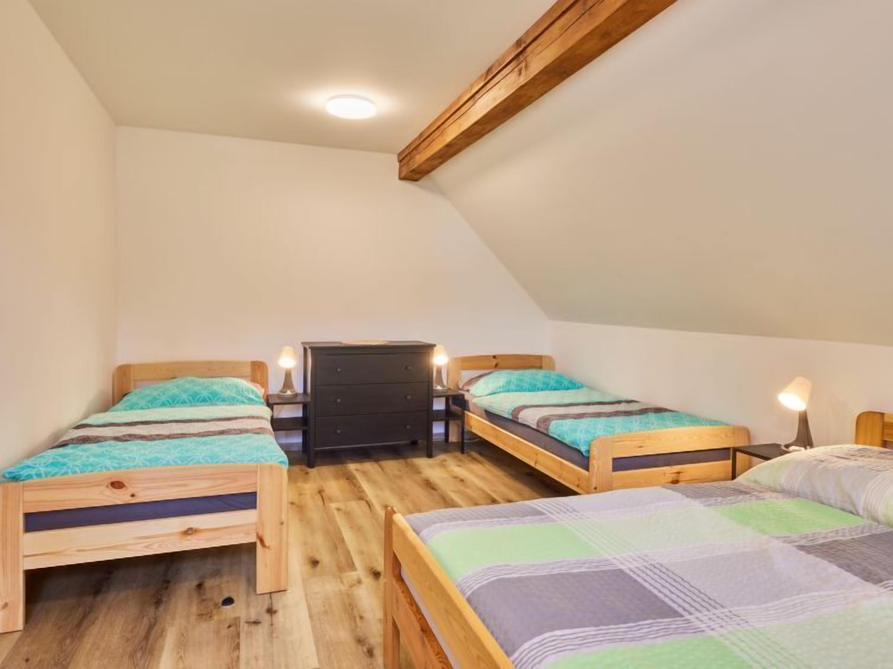 A dormitory room with two wooden bunk beds, a small black dresser, and a ceiling light.