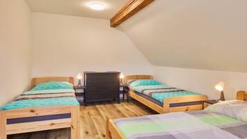 A dormitory room with two wooden bunk beds, a small black dresser, and a ceiling light.