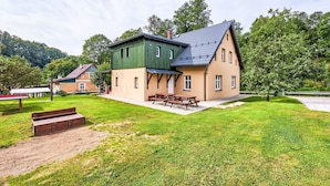 A two-story house with a green exterior and a beige lower level, featuring a patio with a picnic table and benches. - Apartment Meda by Interhome (Rudnik)