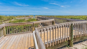 Een houten looppad met leuningen, dat uitkomt op een strand met schaarse begroeiing.