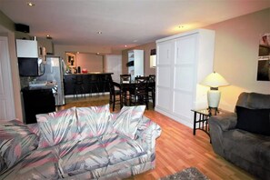 A living room with a sofa, a dining area with chairs, a kitchen with appliances, and a lamp.