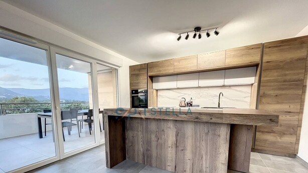 Une cuisine moderne avec un îlot central en bois, un four encastré et une grande fenêtre donnant sur un balcon.