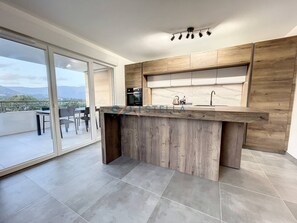 A modern kitchen with a wooden island, a built-in oven, and a large window overlooking a balcony. - Appartement Offrant une Belle vue Dégagée (AJACCIO)