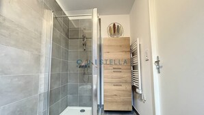 Une salle de bain moderne avec une douche à parois de verre, des carreaux gris, un meuble en bois et une porte blanche.
