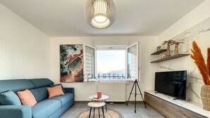 Un salon moderne avec un canapé, un téléviseur, une petite table et une grande fenêtre.