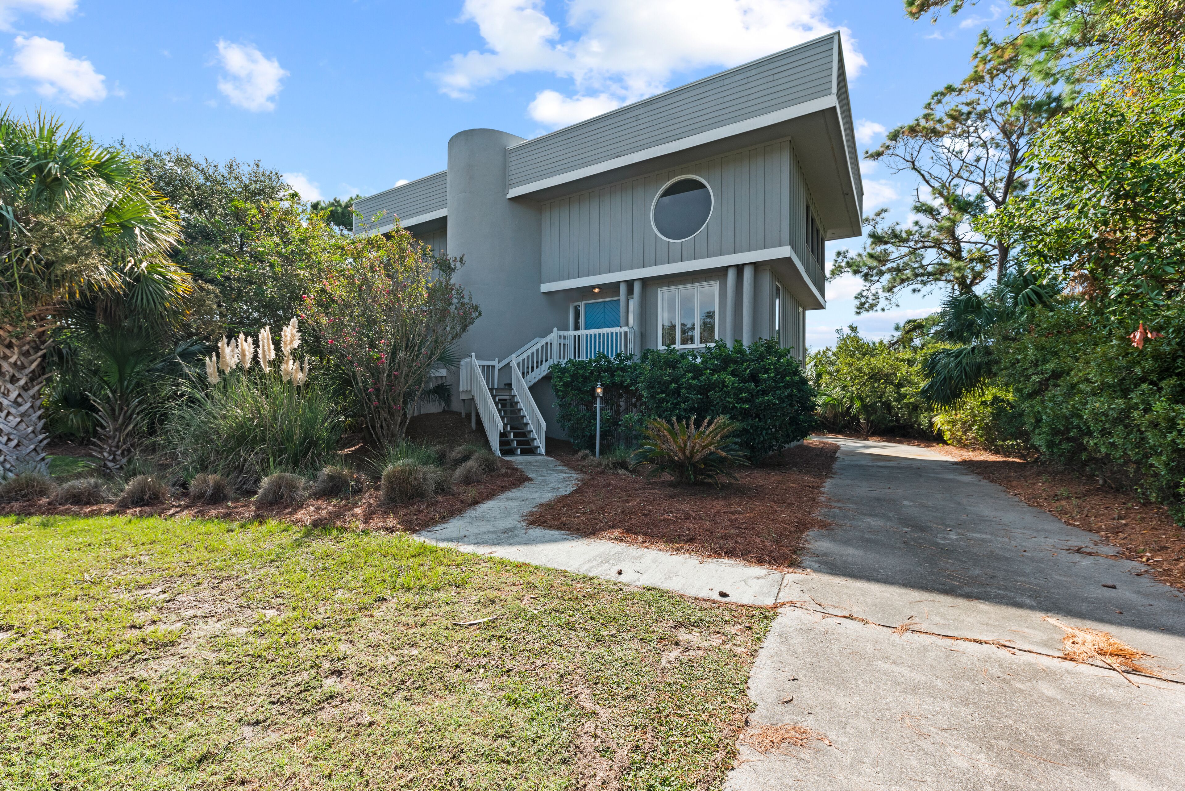 A modern two-story house with a covered porch, a staircase leading to the entrance, and a well-maintained garden with various plants and shrubs.