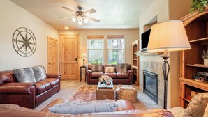 A living room with leather sofas, a fireplace, a ceiling fan, and a large window. - 2BR Cozy Getaway Awaits with High-Speed Wi-Fi! (Park City)