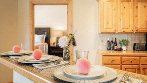 A kitchen with wooden cabinets, a marble countertop, and a dining area with plates, glasses, and utensils. - 2BR Cozy Getaway Awaits with High-Speed Wi-Fi! (Park City)