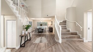 A spacious interior with a central dining area, a staircase leading to an upper level, and a large window providing natural light. - Sunset Paradise l Waterslide l Heated Pool l Hot Tub l Putting Green (Scottsdale)