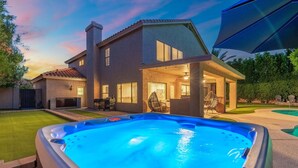 A residential setting with a swimming pool, a covered patio, and a house with a visible chimney. - Sunset Paradise l Waterslide l Heated Pool l Hot Tub l Putting Green (Scottsdale)