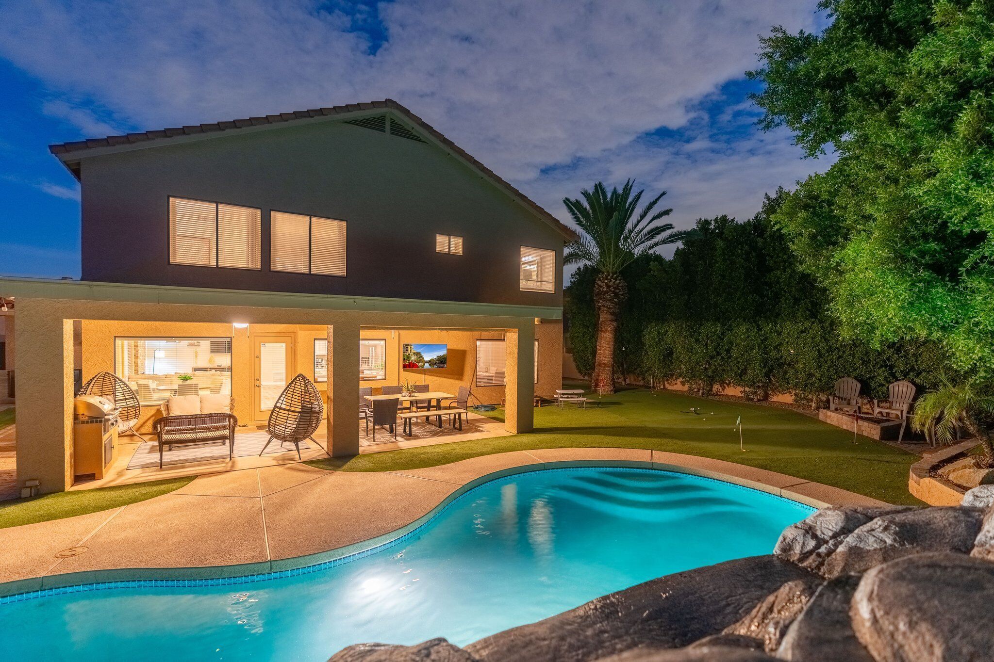 A modern two-story house with a swimming pool, outdoor furniture, and a well-maintained lawn.