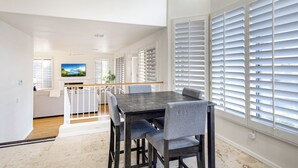 A modern dining area with a dark wooden table and grey upholstered chairs, large windows with white blinds, and a view of a balcony. - Cactus Grove l Heated Pool l Putting Green l BBQ (Scottsdale)