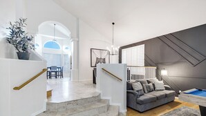 A modern living room with a grey sofa, a pool table, and a staircase leading to another room. - Cactus Grove l Heated Pool l Putting Green l BBQ (Scottsdale)