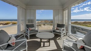 A covered outdoor seating area with white furniture and a view of the beach. - Royal Shell North | Oceanfront | Private Pool and Hot Tub (Virginia Beach)