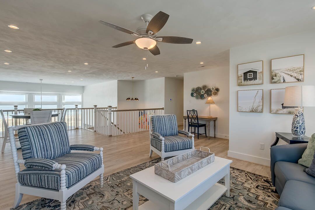 A spacious living area with two striped armchairs, a white coffee table, and a ceiling fan.