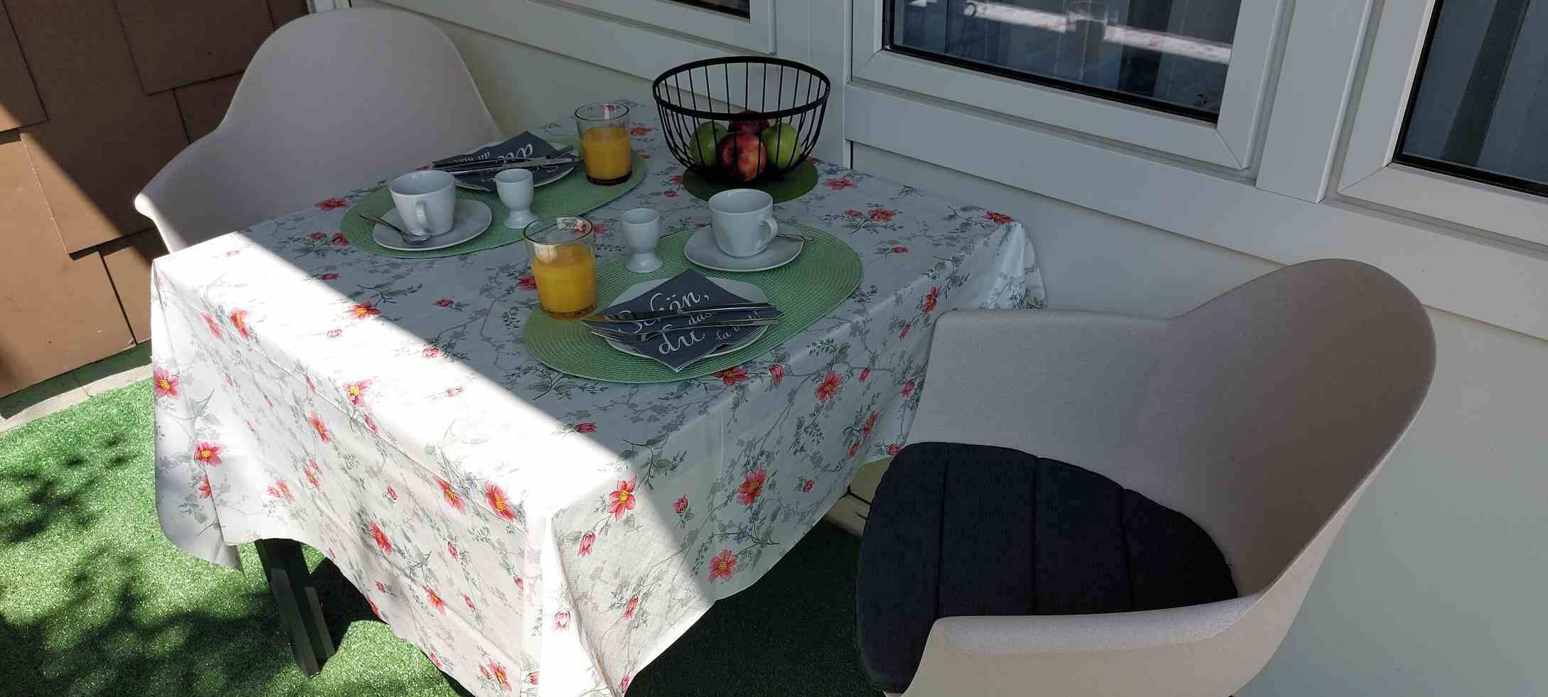 Una mesa de comedor con mantel floral, posavasos verdes y una cesta de frutas.