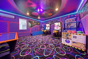 Une pièce décorée sur le thème de l’espace, avec des néons, un jeu d’arcade de basket-ball et un distributeur automatique.