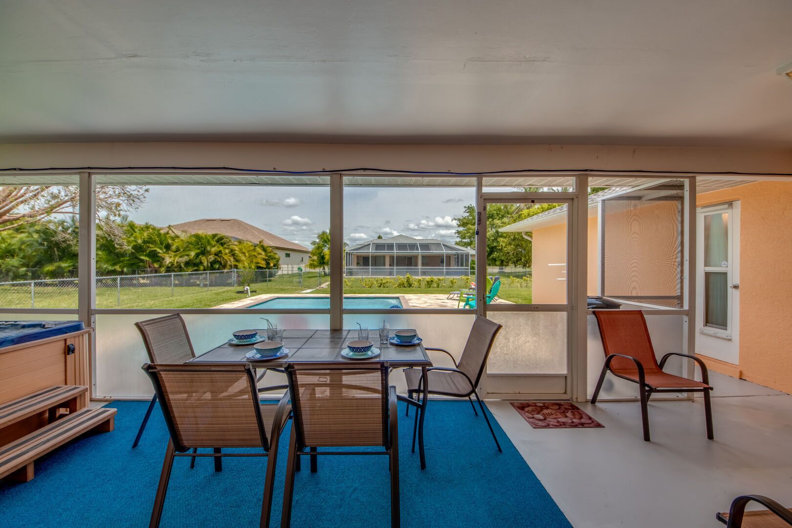 A covered patio with a table set for dining, a pool in the background, and a view of a residential area.