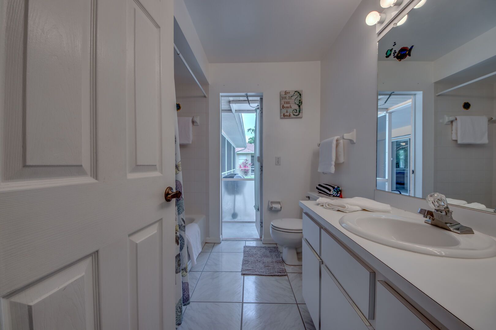 Une salle de bain moderne avec un grand miroir, des éléments d’aménagement blancs et une vue sur l’extérieur.