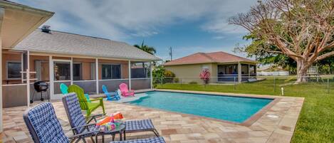 A backyard with a swimming pool, lounge chairs, and a covered patio area.