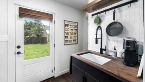 A kitchen with a white door, a framed animal poster, a hanging pot rack, and a coffee maker.