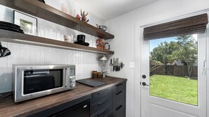 A kitchen with a microwave, wooden shelves, and a door leading to a backyard.