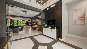 A modern hotel lobby with a reception desk, a chandelier, and a large window. - The Immersive Estate at Reunion - Theme Park Inside Your Vacation Home (Kissimmee)