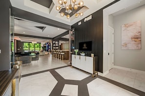 A modern hotel lobby with a reception desk, a chandelier, and a large window.