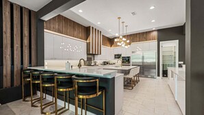 A modern kitchen with a central island, bar stools, and a refrigerator. - The Immersive Estate at Reunion - Theme Park Inside Your Vacation Home (Kissimmee)