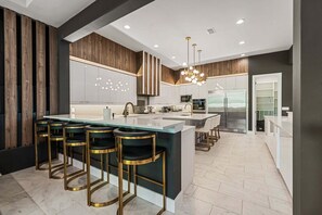A modern kitchen with a central island, bar stools, and a refrigerator.