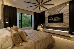 A bedroom with a large bed, a TV mounted on the wall, and a window with curtains.