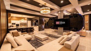 A modern living room with a large flat-screen TV, a sofa, and a coffee table. - The Immersive Estate at Reunion - Theme Park Inside Your Vacation Home (Kissimmee)