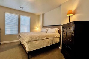 Une chambre à coucher avec un lit, des lampes de chevet, une commode et une fenêtre avec des stores.
