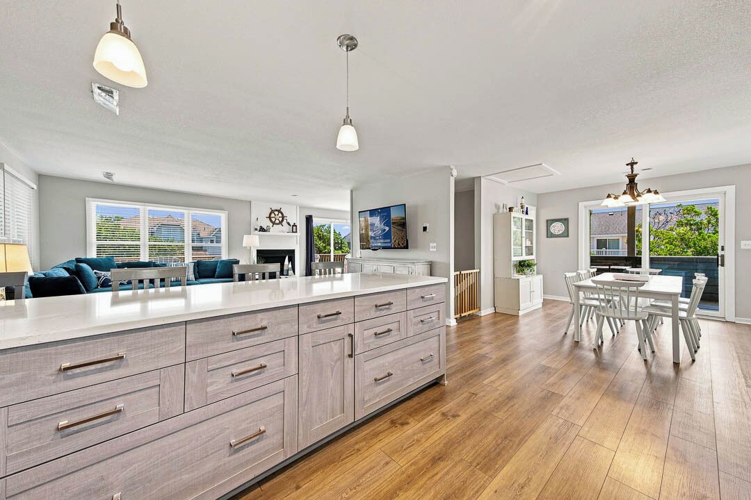 A spacious kitchen with a large island, wooden flooring, and a dining area with white furniture.