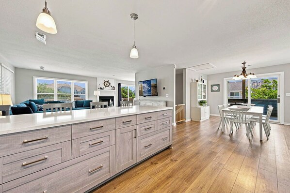 A spacious kitchen with a large island, wooden flooring, and a dining area with white furniture.