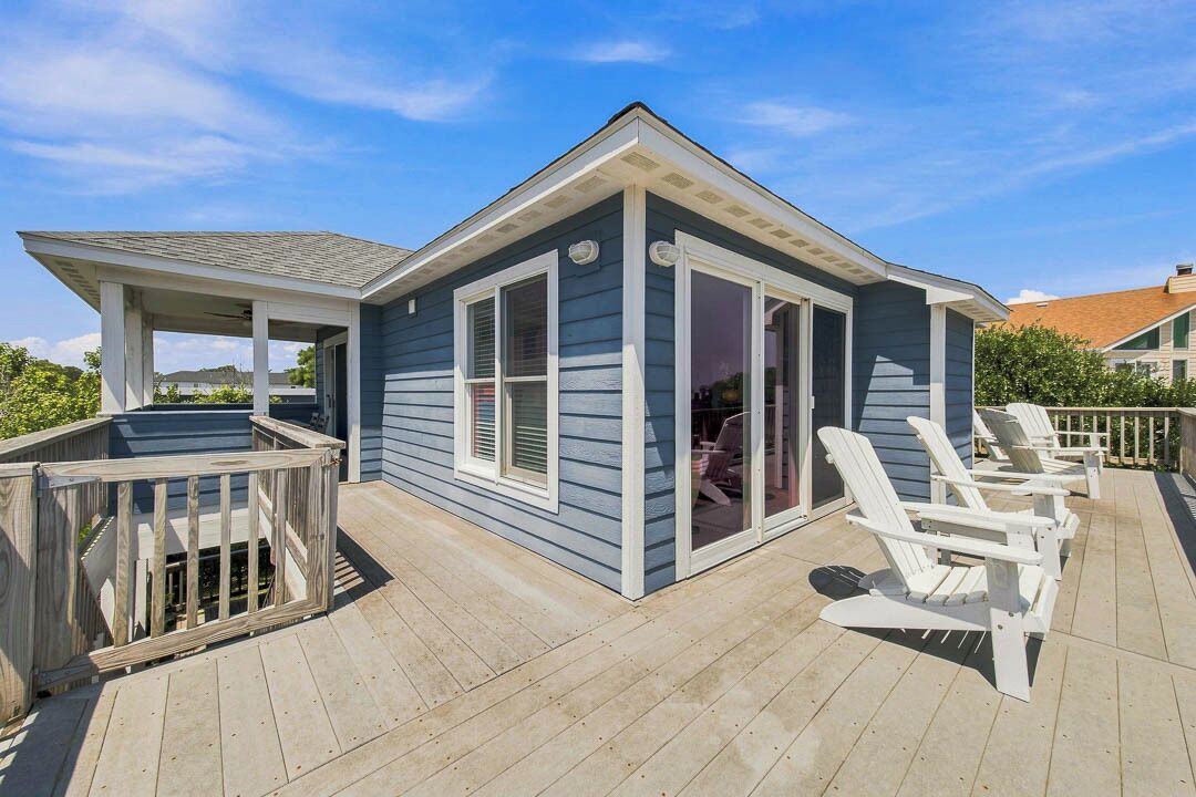 A deck with a covered area, white Adirondack chairs, and a sliding glass door.