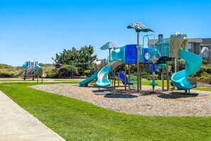 A playground with multiple slides and climbing structures, surrounded by a well-maintained lawn and a clear sky. - Sailors Rest | 844 ft to the beach (Corolla)