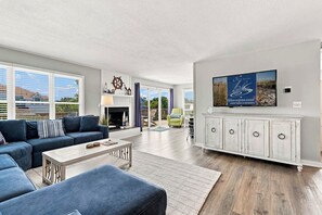 A modern living room with a blue sofa set, a fireplace, and a large TV mounted on a white cabinet.