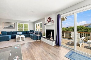 A spacious living room with a sectional sofa, a fireplace, and a large sliding glass door leading to an outdoor deck.