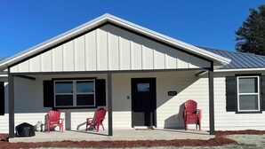 A single-story building with a gabled roof and a covered porch. There are two red Adirondack chairs on the porch. - Beautiful New House on 5 Acres close to springs (High Springs)